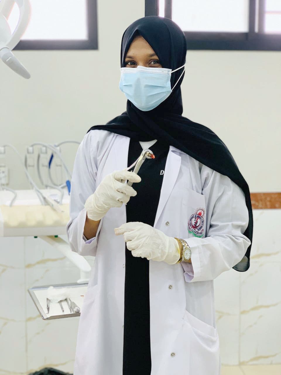 Dentist wearing a hijab and lab coat holding dental forceps with an extracted tooth.